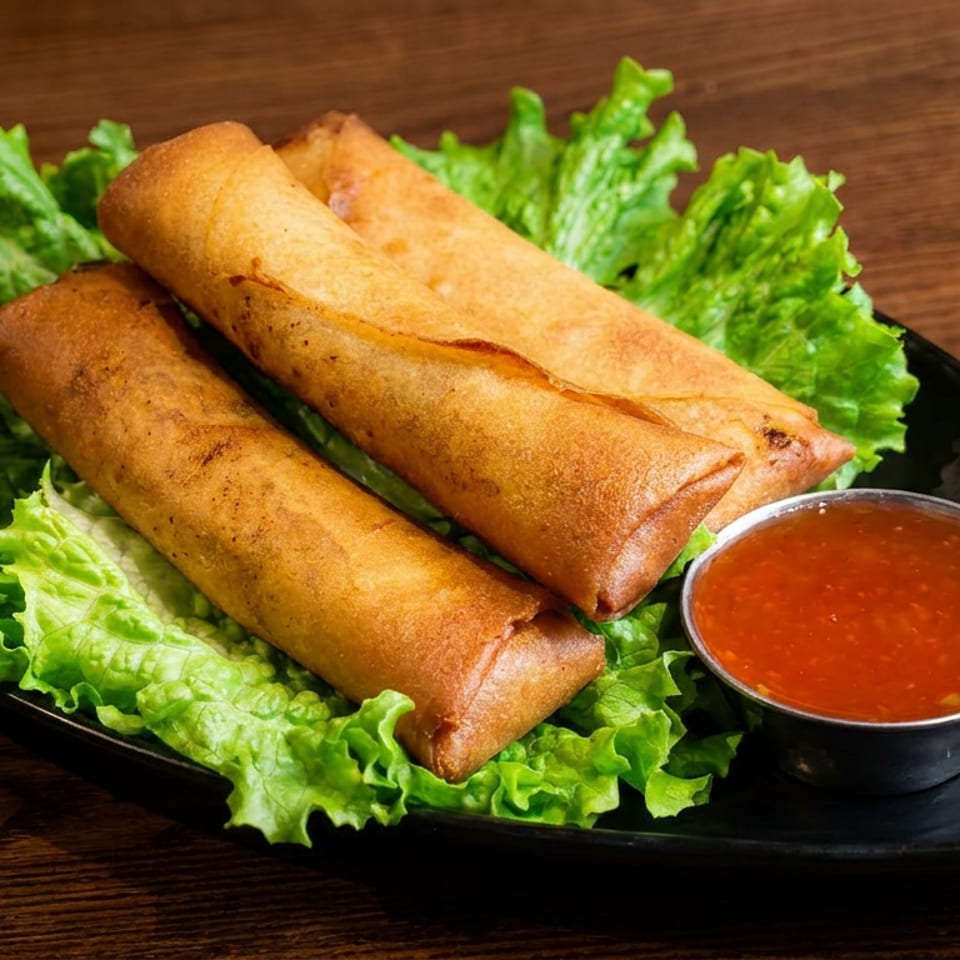 Three crispy spring rolls served on lettuce with a bowl of sweet chili sauce on a black plate.