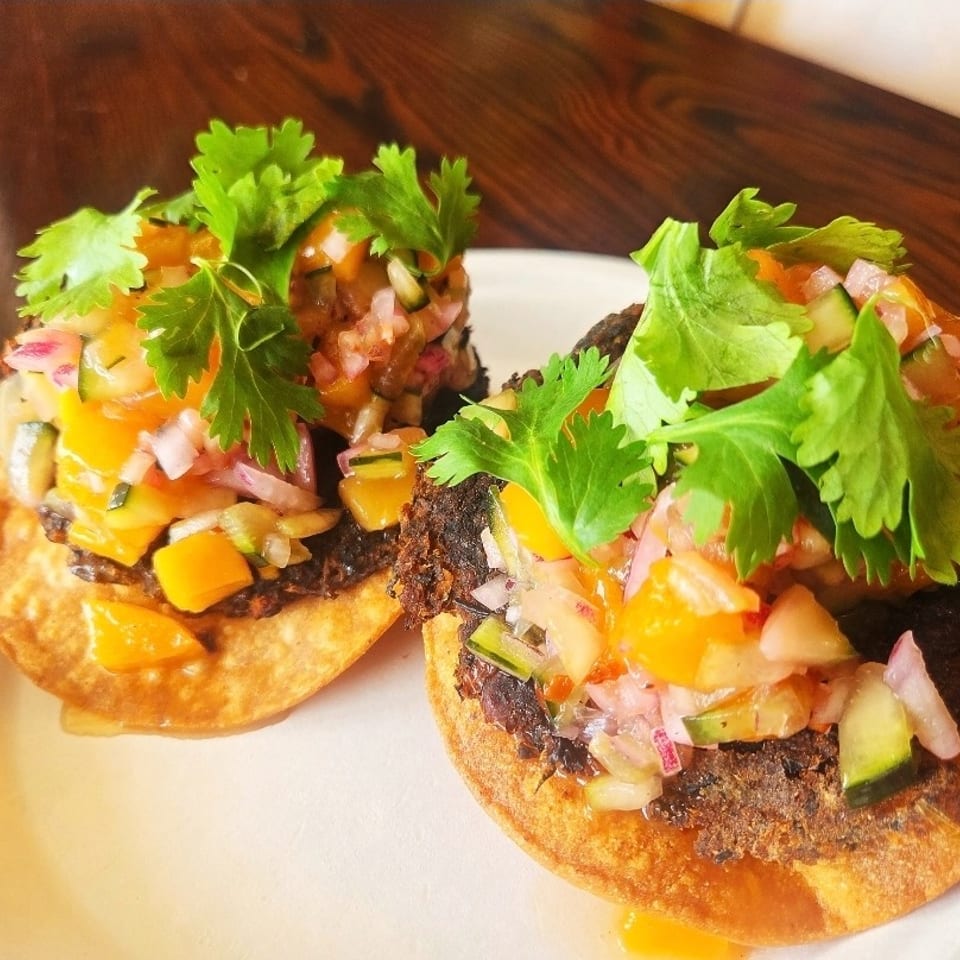 Three crispy tostadas topped with refried beans, diced vegetables, salsa, melted cheese, and fresh cilantro on a white plate.