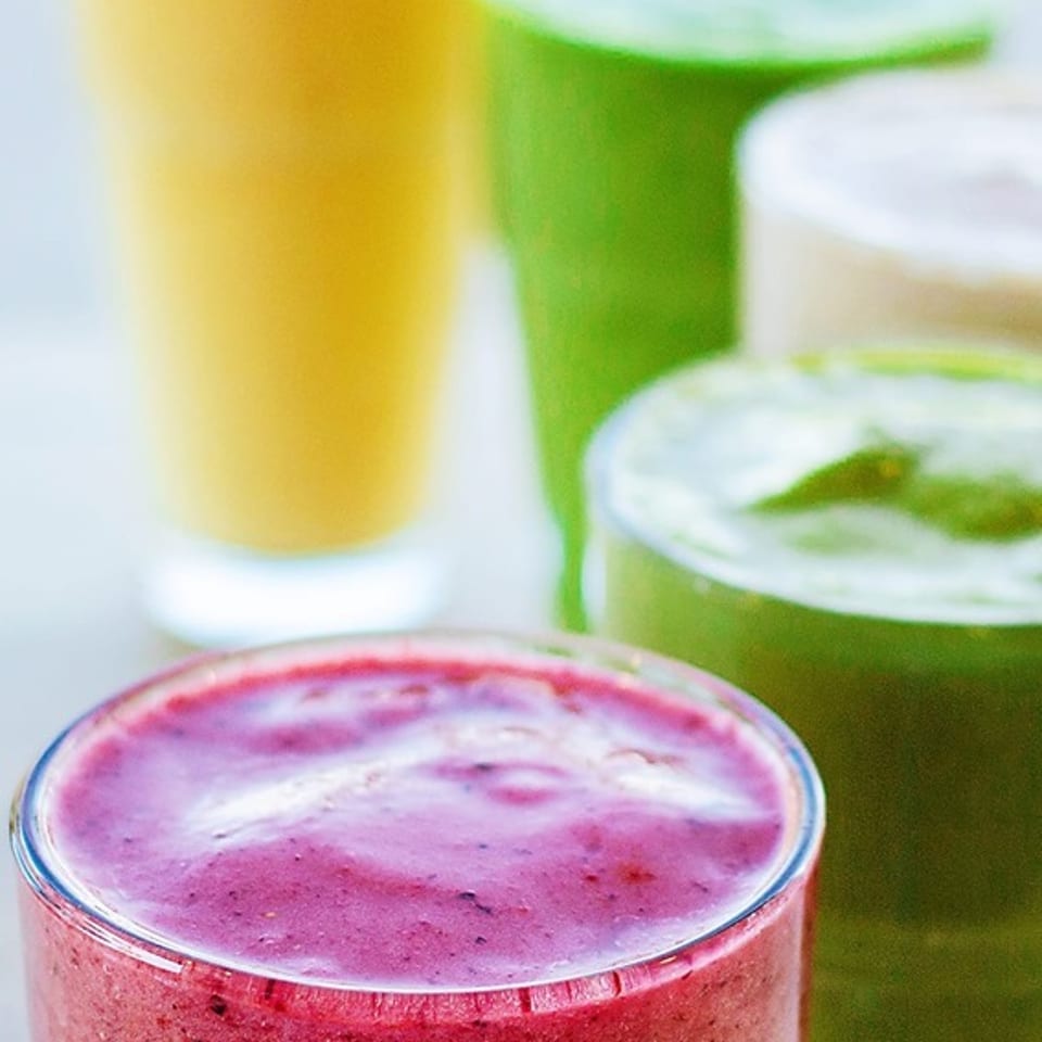 Colorful fruit smoothies in red, green, yellow, and creamy white arranged in clear glasses.